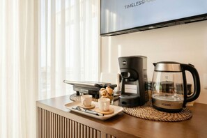 Habitación de hotel con espacio para café, televisión y ventana con cortinas.