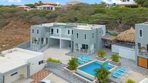 A modern resort with a swimming pool, multiple balconies, and a car parked nearby. - Casa Tortuga – Luxury Holiday Home in Papaya Hill Resort, Cu (Grote Berg)