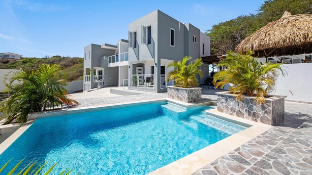 A modern two-story house with a swimming pool, stone planters, and a thatched roof structure. - Casa Tortuga – Luxury Holiday Home in Papaya Hill Resort, Cu (Grote Berg)