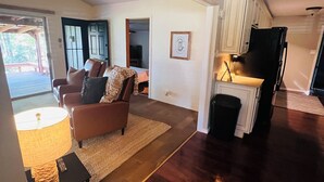 A spacious living room with a large window, a fireplace, a dining area with a kitchen, and a door leading to an outdoor deck.