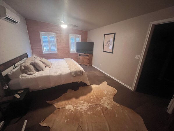 Une chambre à coucher avec un lit, un téléviseur, un tableau encadré au mur et une porte.