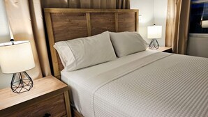 Un lit bien fait, avec une tête de lit en bois, deux tables de chevet avec des lampes et une commode en bois dotée de tiroirs.