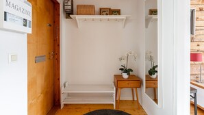 Ein Flur mit Holztür, einer weißen Bank, einem kleinen Tisch mit Orchidee im Topf und einem Regal mit gerahmten Bildern.