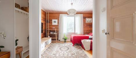 A cozy bedroom with a wooden ceiling, a red bed, and a small window.