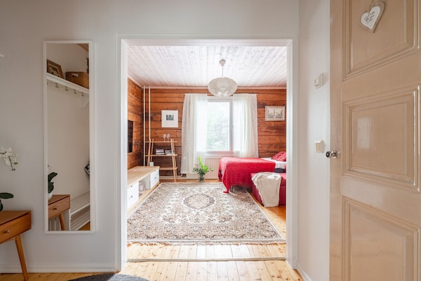 A cozy bedroom with a wooden ceiling, a red bed, and a small window.