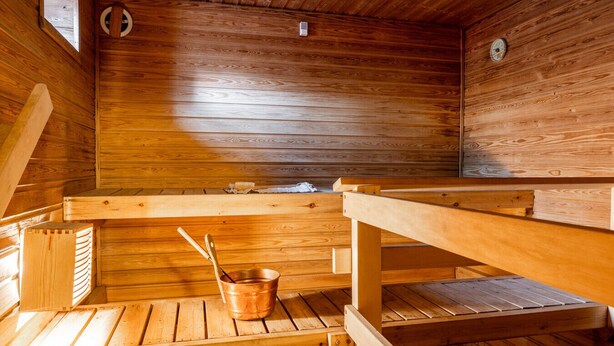Eine Holzsauna mit Bänken, einem Eimer und einem kleinen Ofen.