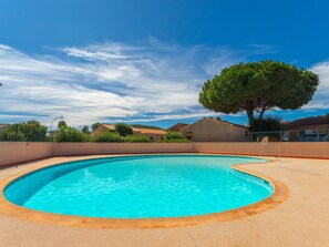 A swimming pool with a curved edge, surrounded by a sandy area and a low wall.
