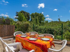 A table set outdoors with a red tablecloth, surrounded by white chairs, under a clear blue sky.