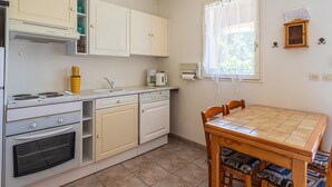 A compact kitchen with white cabinets, a stove, oven, and a dining table with chairs. - Les Mimosanes by Interhome (Bormes-les-Mimosas)