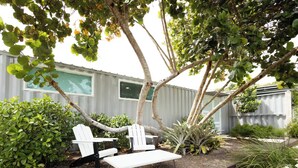 A patio with two white Adirondack chairs, a small table, and a variety of plants and shrubs. - 3-bedroom 4 Bathrooms Solar Panels, Pool, Near Beaches, Vega Alta / Dorado (Vega Alta)