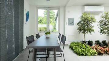 A modern meeting room with a long table, black chairs, a potted plant, and a view of greenery outside.
