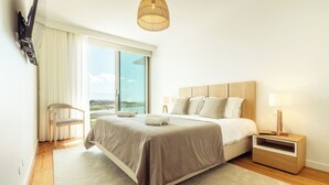 A modern hotel room with a large bed, a nightstand, a chair, and a view of the outdoors. - Bayline Algarve Apt – Beachfront, Spa, Lagoon View (Armação de Pêra)