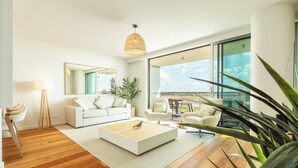 A modern living room with a white sofa, a coffee table, and a dining area with a wooden floor. - Bayline Algarve Apt – Beachfront, Spa, Lagoon View (Armação de Pêra)