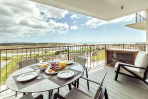 Un balcon avec une table préparée pour le petit-déjeuner, offrant une vue sur un paysage côtier.