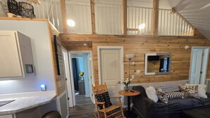 A cozy interior with a wooden ceiling, a sofa, a rocking chair, and a small table with a vase and a remote control.