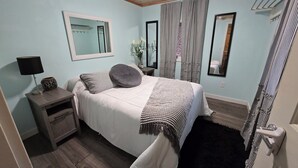 A bedroom with a bed, bedside table, lamp, and a mirror.