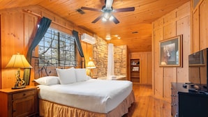 Ein Schlafzimmer in einer Holzhütte mit einem Bett, Nachttischen, einem Deckenventilator und einer Steinwand.