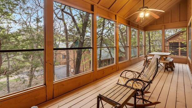 Eine Holzterrasse mit großen Fenstern, einem Deckenventilator und einem Tisch mit Stühlen.