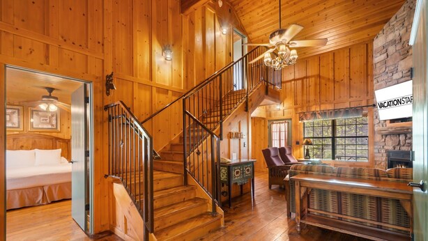 A wooden interior with a staircase, a bed, a fireplace, and a sign reading "VACATION STARTS HERE".