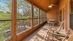 A wooden deck with large windows, wooden chairs, and a ceiling fan.