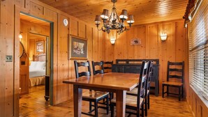 A wooden dining room with a large table and chairs, a chandelier, and a wall-mounted light fixture.