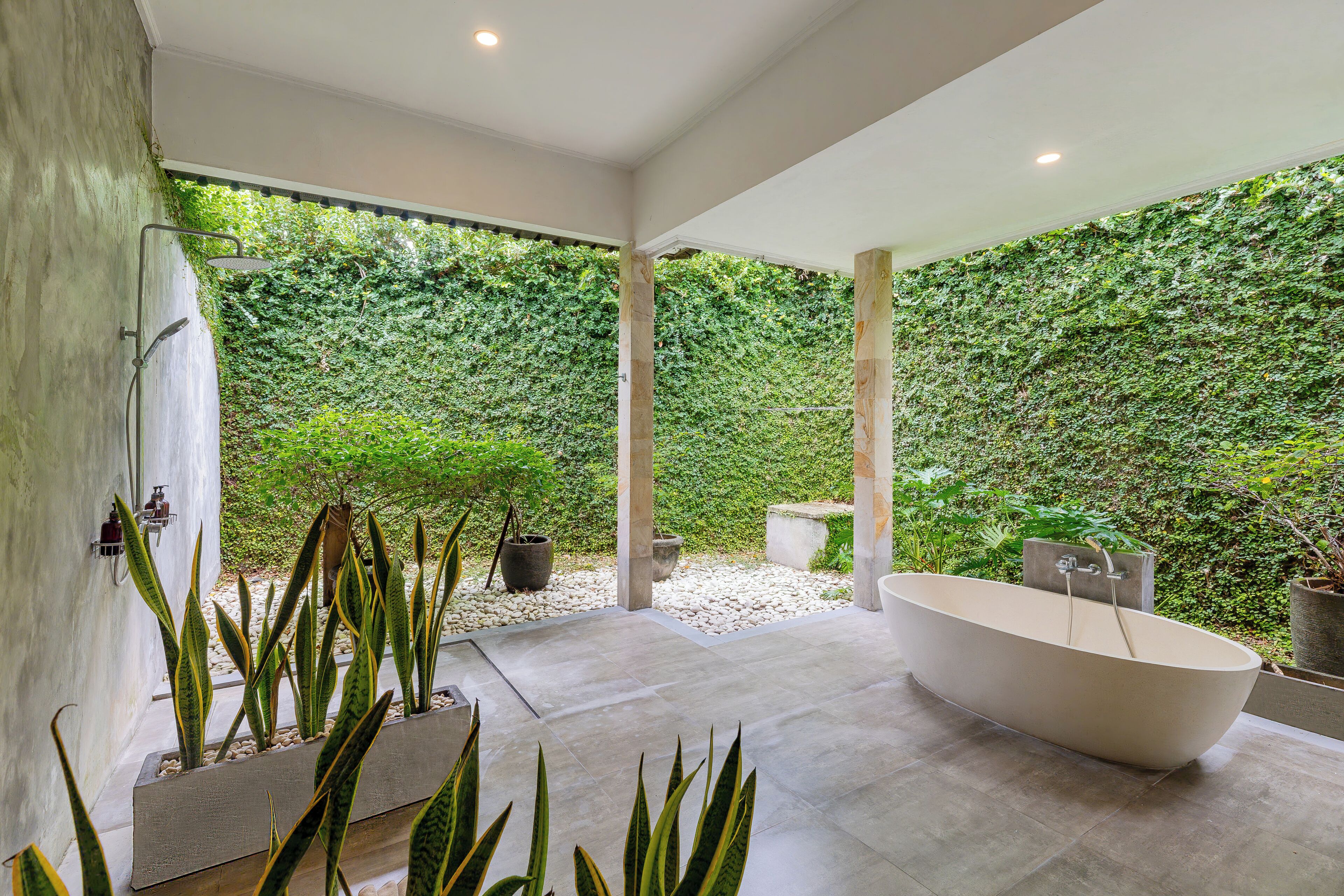 A modern bathroom with a freestanding bathtub, a shower, and a large window overlooking a lush green wall.