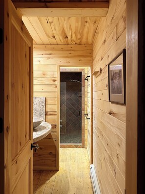 A wooden cabin interior with a bathroom featuring a marble sink, a shower with a glass door, and a framed picture on the wall. - Skyline Ranch (Cloudcroft)