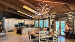 A rustic cabin interior with a wooden dining area, a kitchen with wooden cabinets, and a unique antler chandelier.