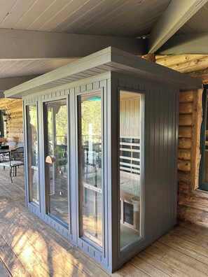 A modern log cabin with a covered porch, large sliding glass doors, and a wooden deck. - Skyline Ranch (Cloudcroft)