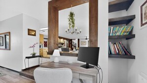 Un salon moderne avec un bureau en bois, un ordinateur, une bibliothèque et une plante suspendue.