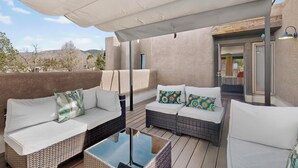 Un espace extérieur aménagé, abrité et doté de mobilier en osier et de coussins, ainsi qu’une table en verre, offrant une vue sur le paysage environnant.