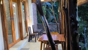 An outdoor dining area with wooden tables and chairs, surrounded by natural elements and a stone wall. - Ganayu Bali Villa (Gobleg)