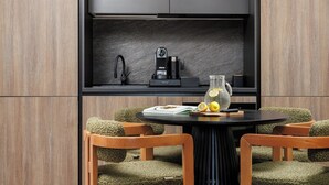 Una cocina moderna con cafetera integrada, hervidor y una jarra de limones sobre una mesa redonda con dos sillas.