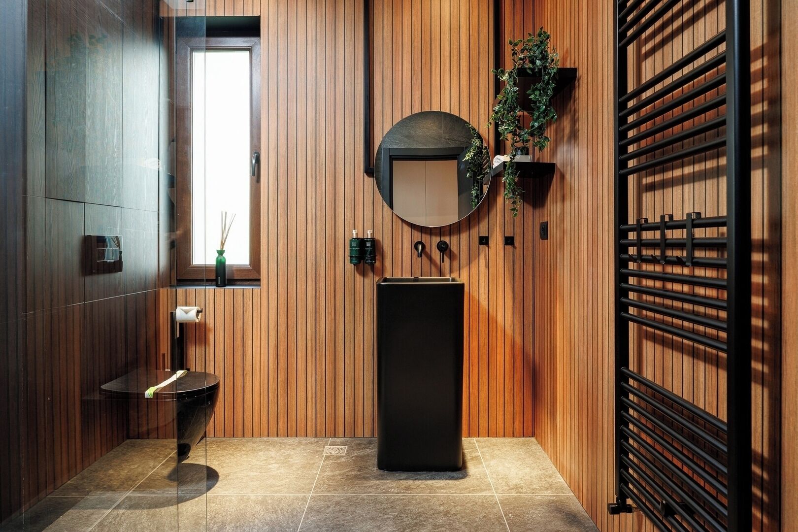 Un baño moderno con paneles de madera, un espejo redondo, un lavamanos negro y un perchero para toallas.