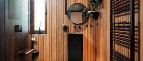 Un baño moderno con paneles de madera, un espejo redondo, un lavamanos negro y un perchero para toallas.