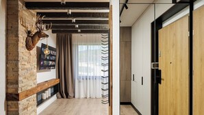 Een gang met een stenen muur, een opgehangen hertenkop, een houten plank en een doorkijk naar een kamer met een deur.