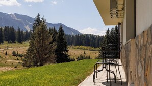 Een balkon met een tafel en stoelen met uitzicht op een bergachtig landschap met bomen.