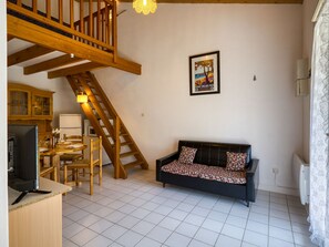 A living room with a wooden staircase, a sofa, a dining table with chairs, and a kitchen area.