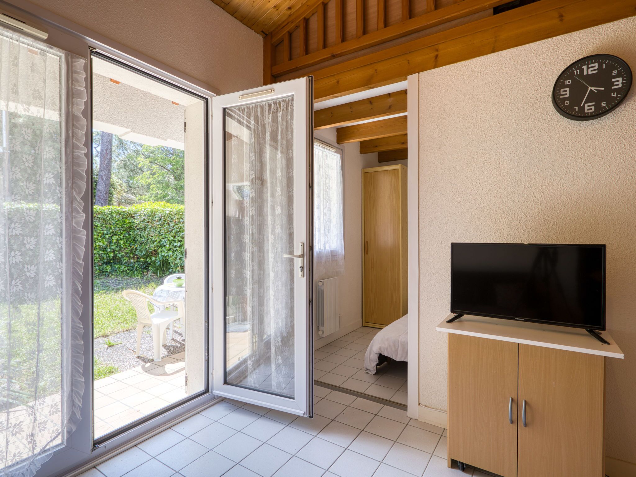 A room with a sliding glass door leading to a patio, a bed, a TV on a stand, and a clock on the wall.