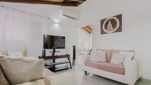 Ein Wohnzimmer mit einem weißen Sofa, einem Fernseher und einem an der Wand hängenden Kunstwerk.