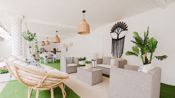 Ein modernes Wohnzimmer mit einem Korbstuhl, grauen Sofas und einem Couchtisch. Es gibt hängende Korbstrahler und eine Wanddeko aus Makramee.