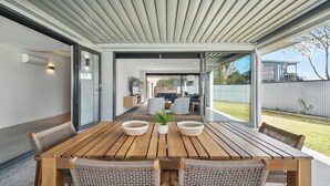 A modern dining area with a wooden table and wicker chairs, large windows, and a view of the backyard.