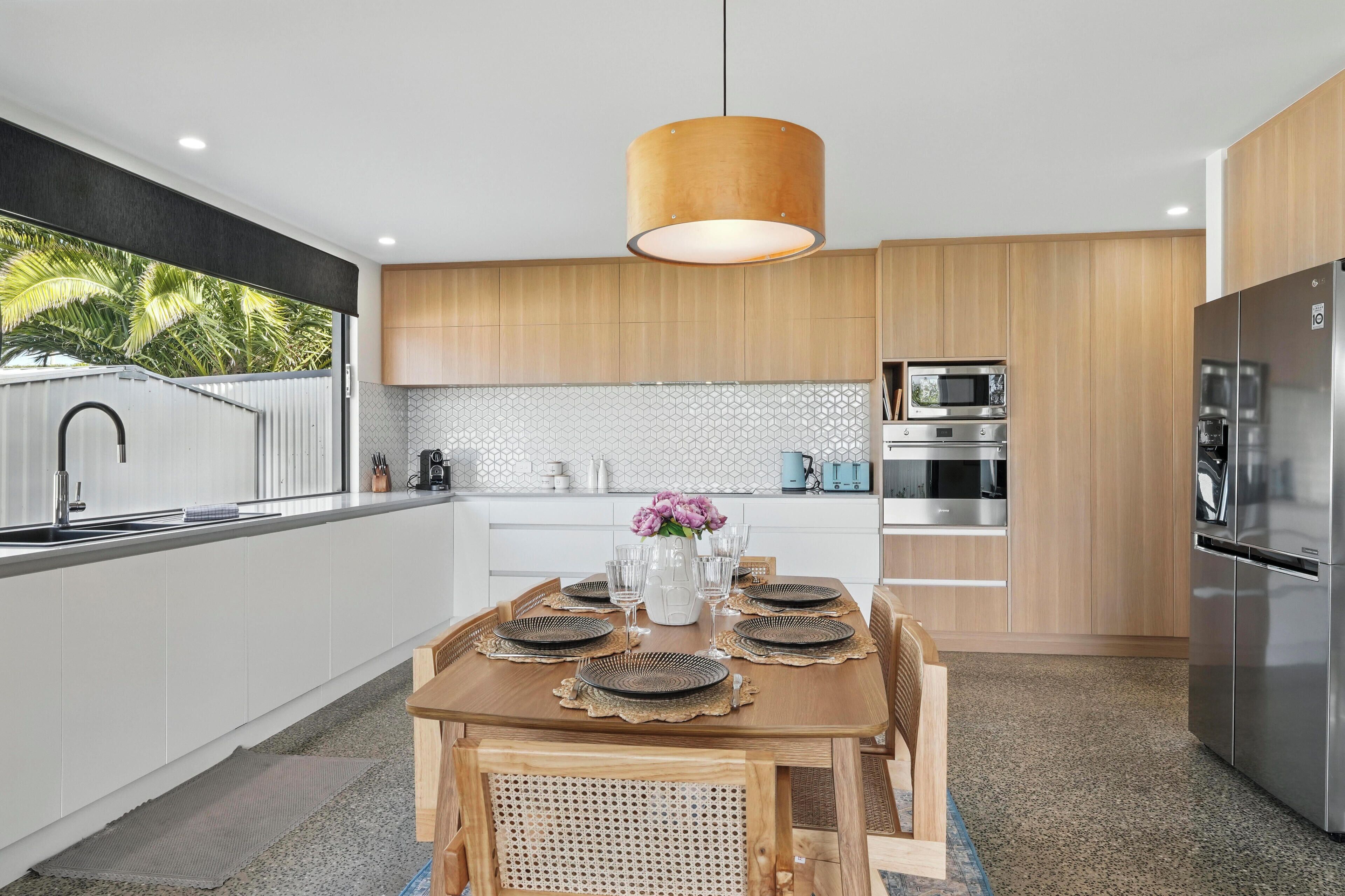 Una cocina moderna con armarios de madera, un refrigerador de acero inoxidable y una mesa de comedor lista para seis personas.