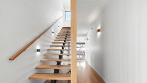 A modern staircase with wooden steps and a glass railing, leading to a bright room with a view of the outdoors.