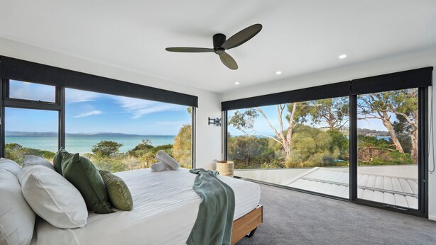 A bedroom with a large bed, a ceiling fan, and a view of the ocean.