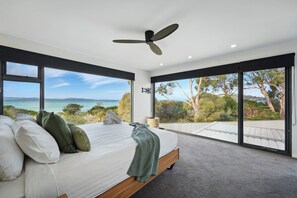 A bedroom with a large bed, a ceiling fan, and a view of the ocean. - Beautiful Balook - 3 Bedroom Beach House (Lauderdale)