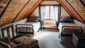 A small attic bedroom with two beds, a bench, and a chair.