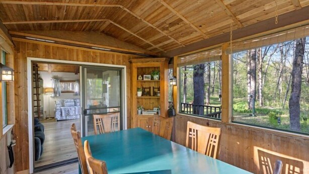 A wooden cabin with a dining area, a kitchen, and a view of the forest.