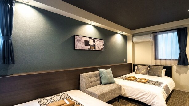 Una habitación de hotel con dos camas, un sofá, una obra de arte colgada en la pared y una ventana con cortinas.