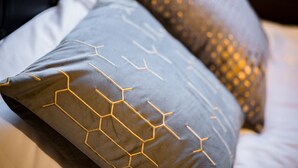 Primer plano de una cama con un cojín de estampado gris y dorado, y un cojín texturizado con motivos dorados.
